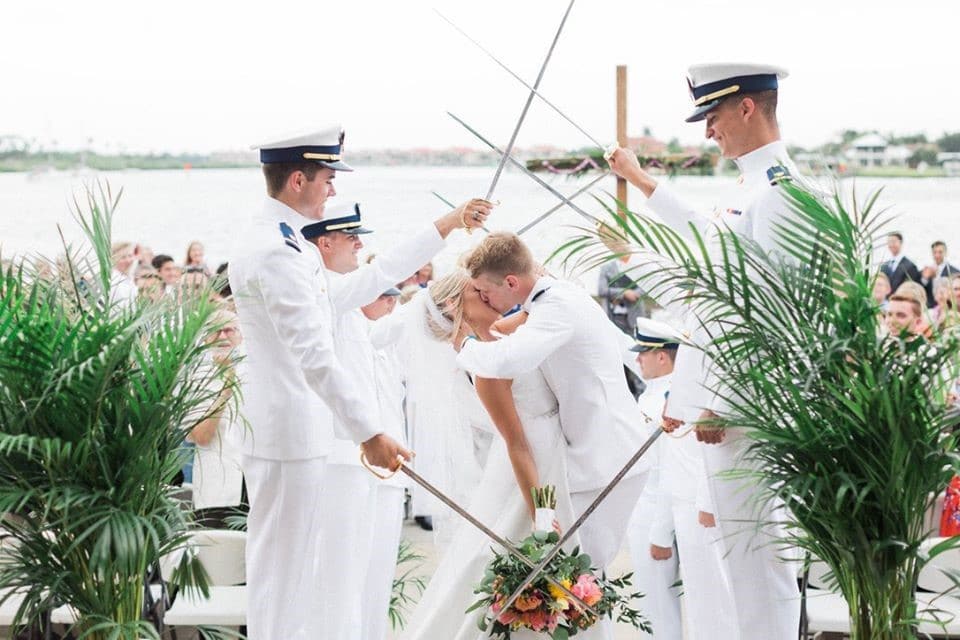 bride and groom kissing at military wedding with officers holding swords next to tropical plants overlooking water